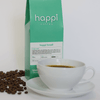 12 oz bag of happi brazil medium roast specialty coffee with scattered beans and brewed coffee in white cup