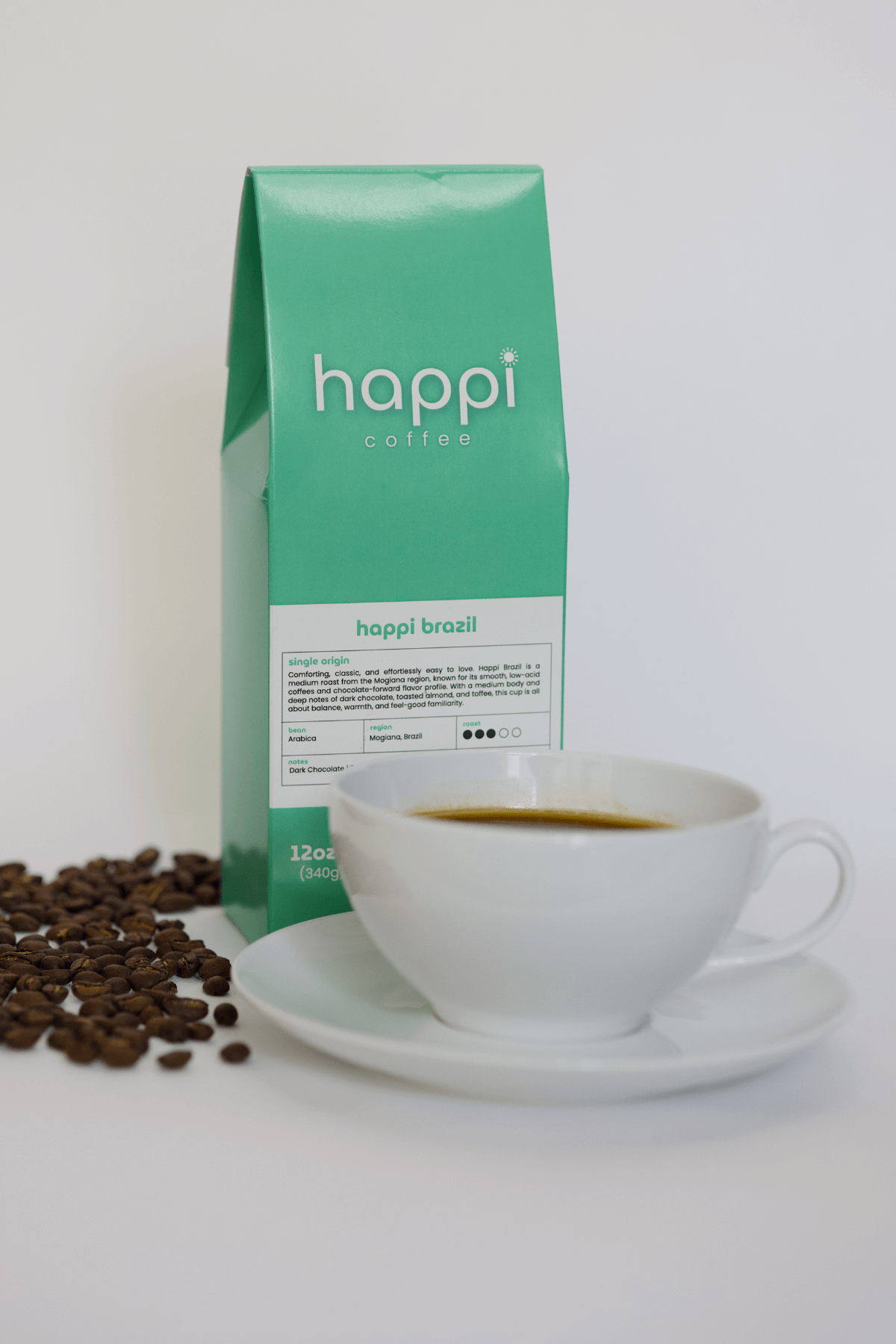 12 oz bag of happi brazil medium roast specialty coffee with scattered beans and brewed coffee in white cup