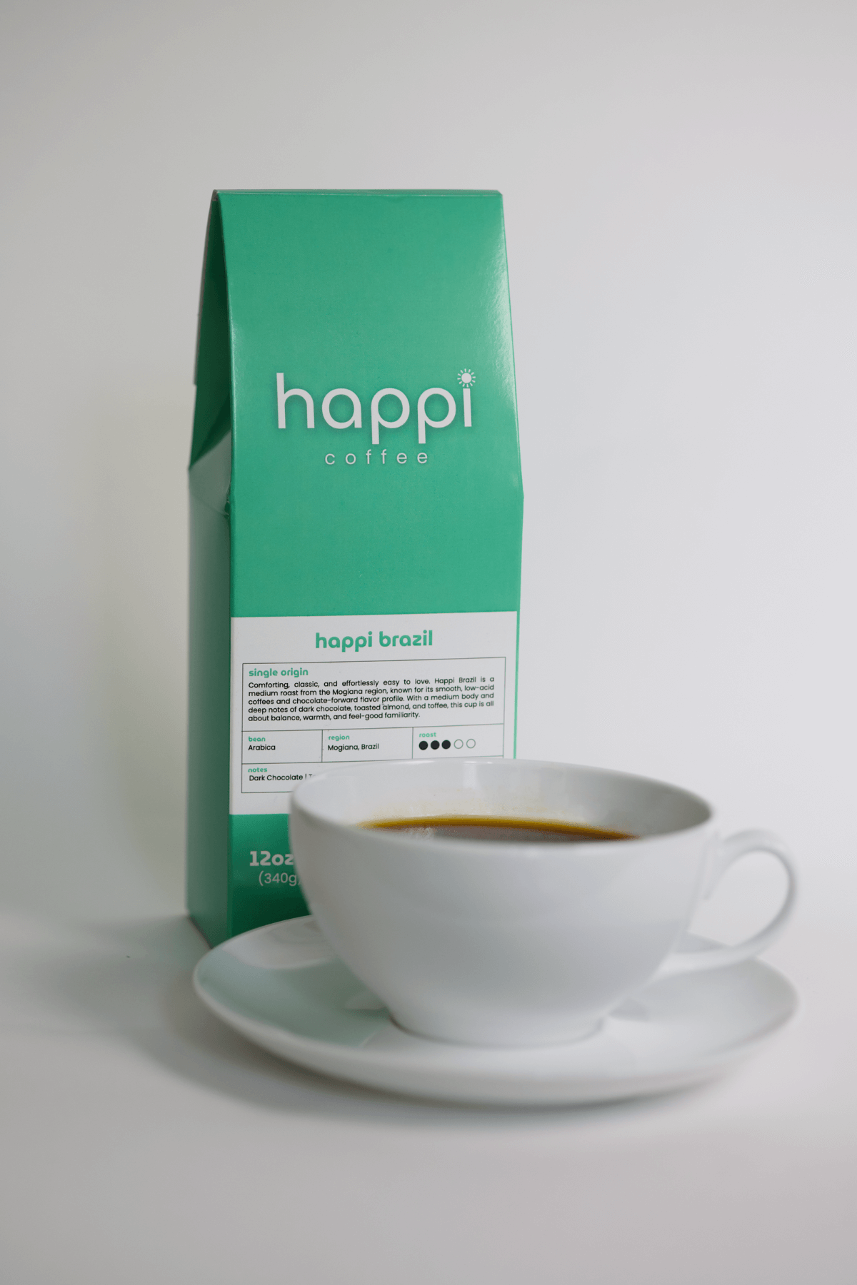 12 oz bag of happi brazil medium roast specialty coffee with brewed coffee in a white cup and saucer