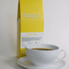 12 oz bag of Happi Bright light roast specialty coffee with brewed coffee in a white cup and saucer