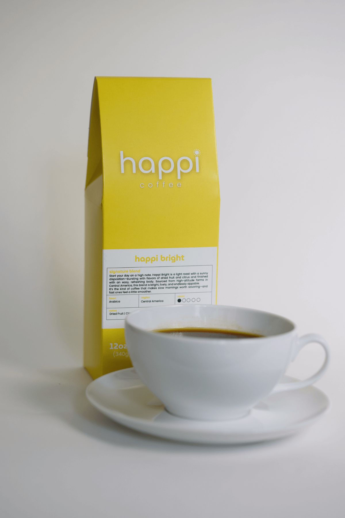 12 oz bag of Happi Bright light roast specialty coffee with brewed coffee in a white cup and saucer