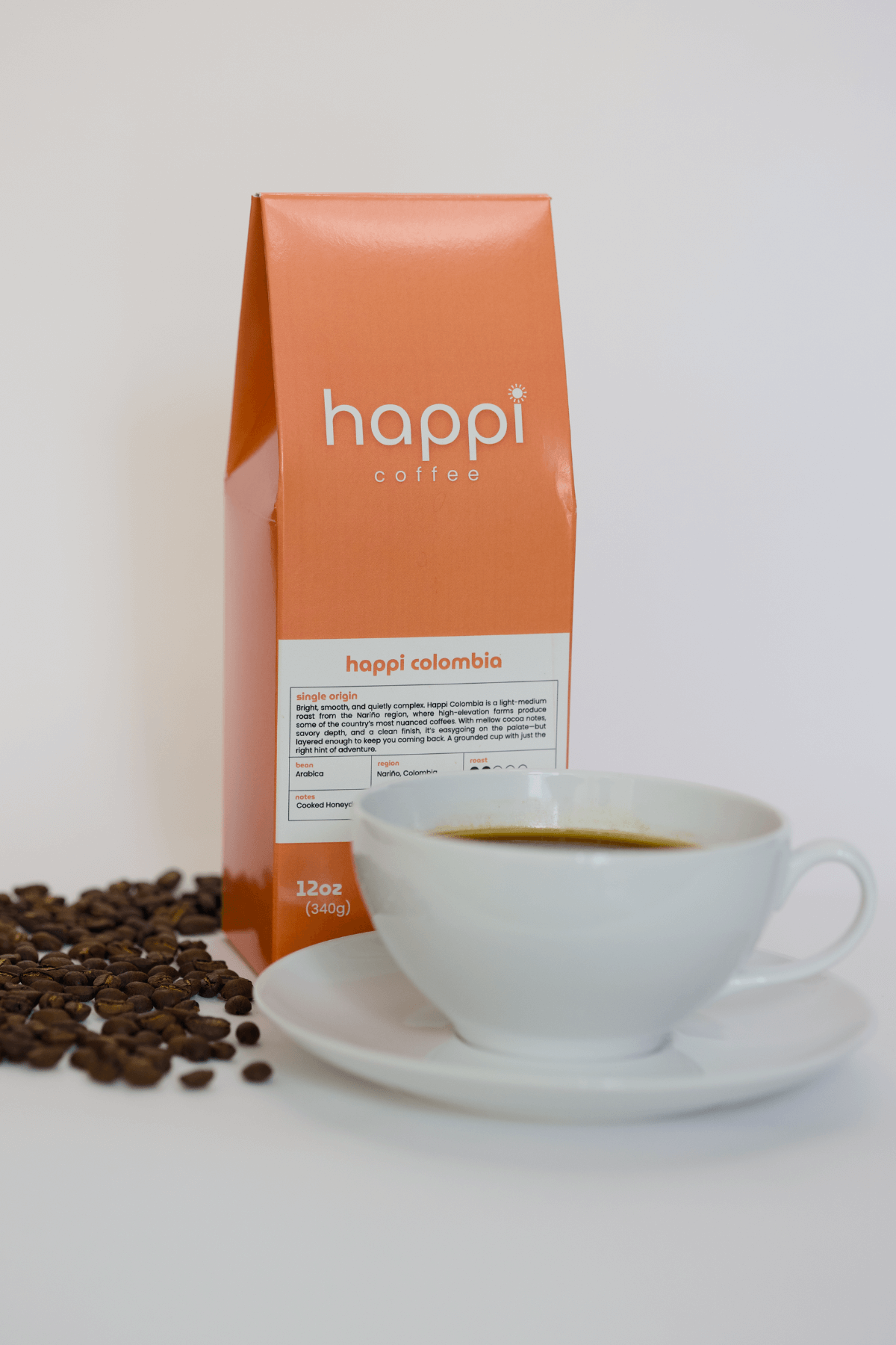 12 oz bag of happi colombia light roast specialty coffee with scattered beans and brewed coffee in white cup