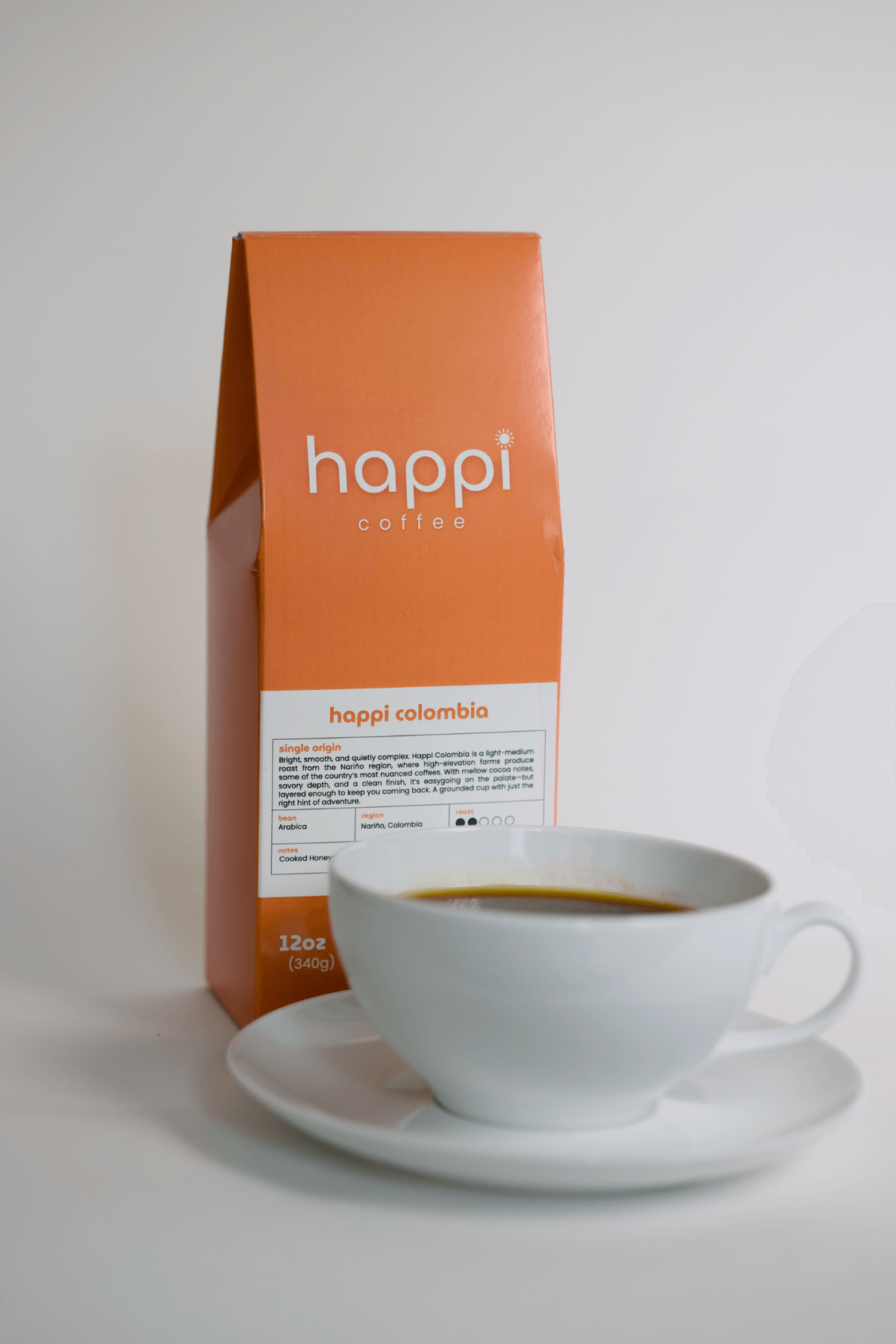 12 oz bag of happi colombia light roast specialty coffee with brewed coffee in a white cup and saucer