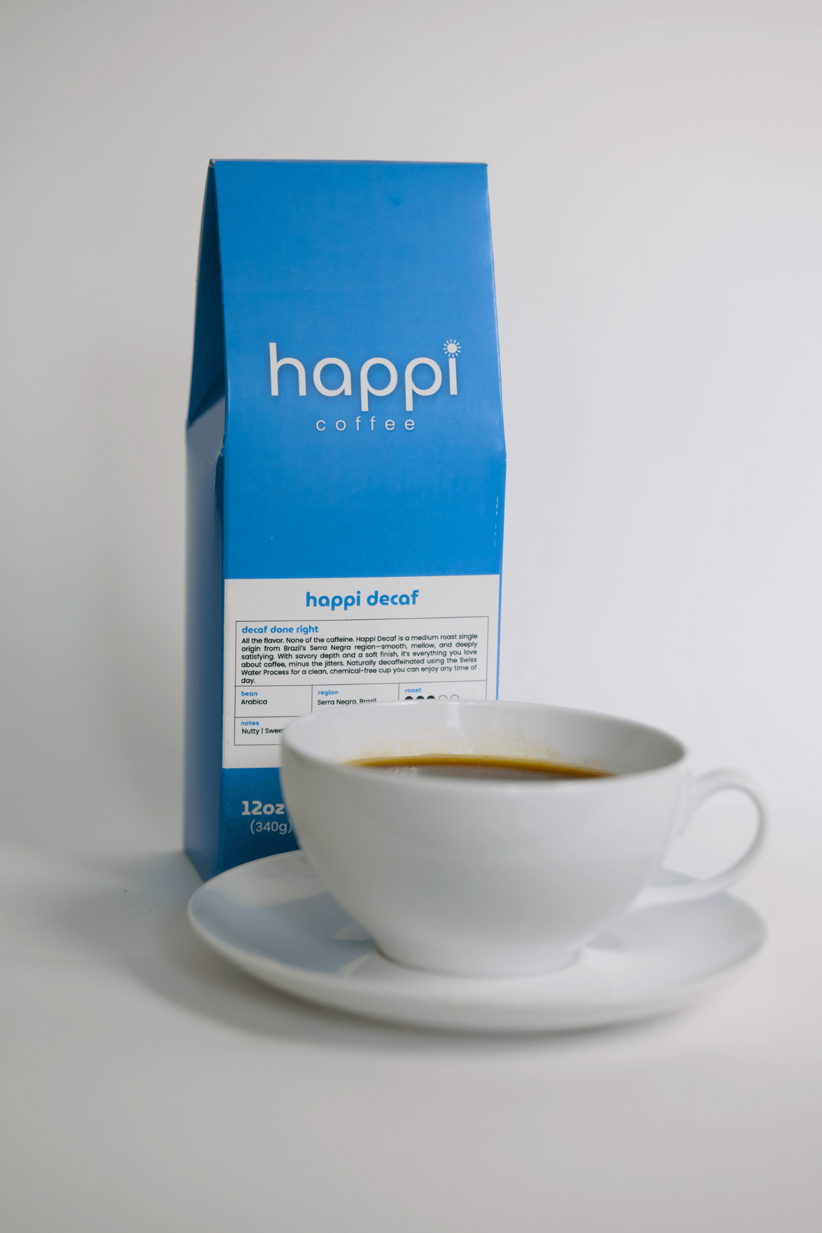 12 oz bag of happi decaf medium roast specialty coffee with brewed coffee in a white cup and saucer