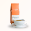 Side view of 12 oz bag of Happi Colombia with cup of coffee. Best Light Roast Coffee Beans with Bright Citrus, Cocoa Warmth & Smooth Body, Available Ground or Whole Bean