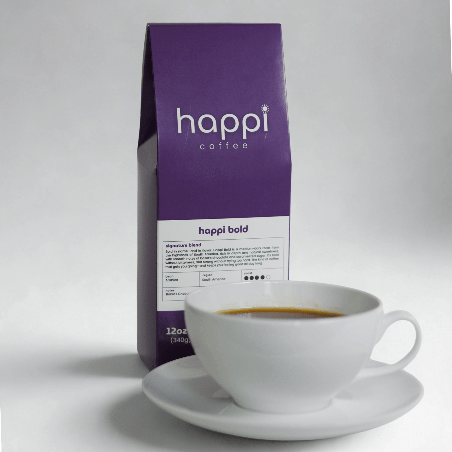 View of 12 oz bag of Happi Bold next to a cup of coffee. Best Dark Roast Coffee Beans with Baker’s Chocolate, Caramel & Deep Body, Available Ground or Whole Bean