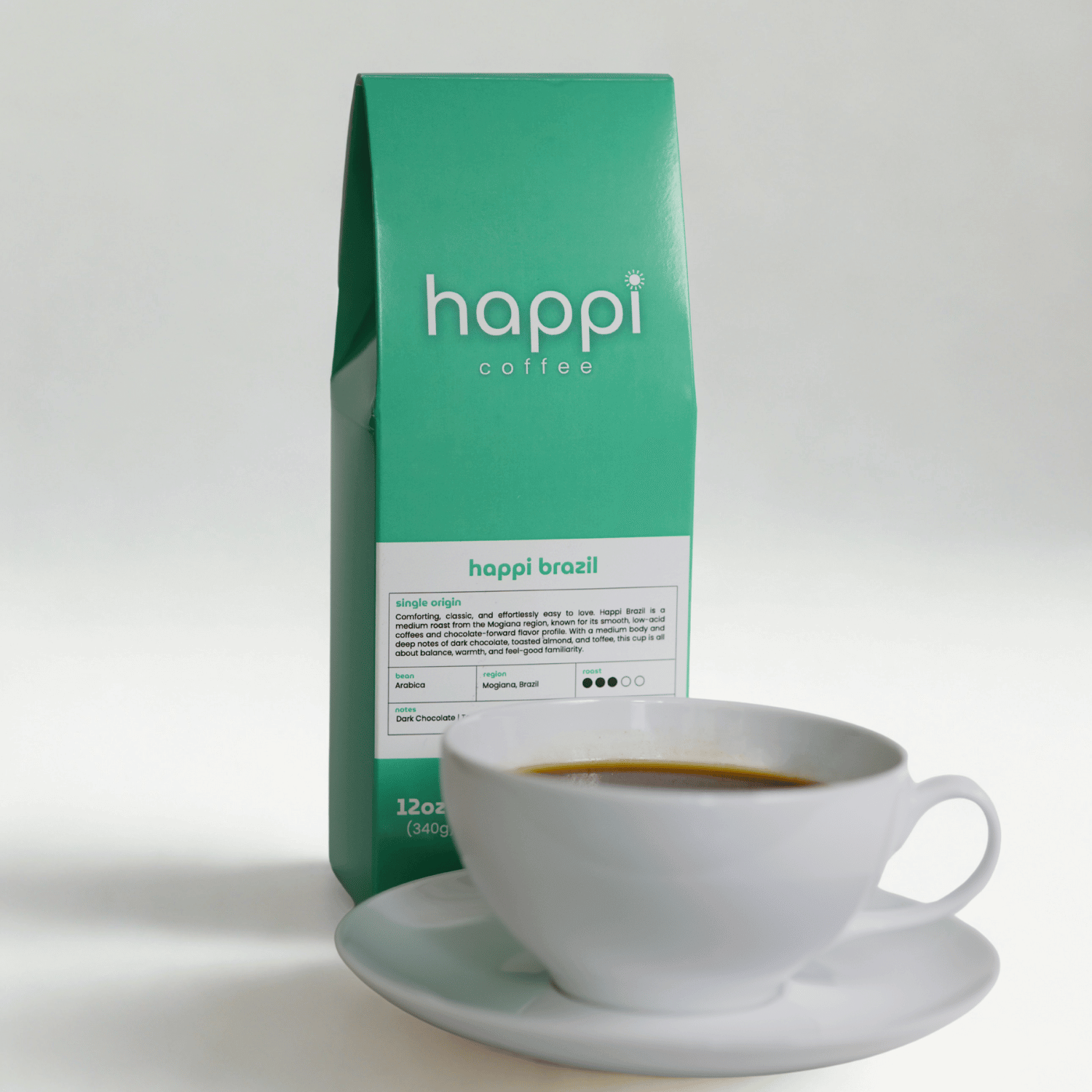 View of 12 oz bag of Happi Brazil next to a cup of coffee. Best Medium Roast Coffee Beans with Chocolate, Almond & Toffee Notes, Available Ground or Whole Bean