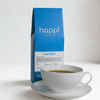 View of 12 oz bag of happi decaf medium roast coffee next to a cup of coffee – available in whole bean or ground