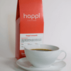 12 oz bag of Happi Smooth medium roast specialty coffee with brewed coffee in a white cup and saucer