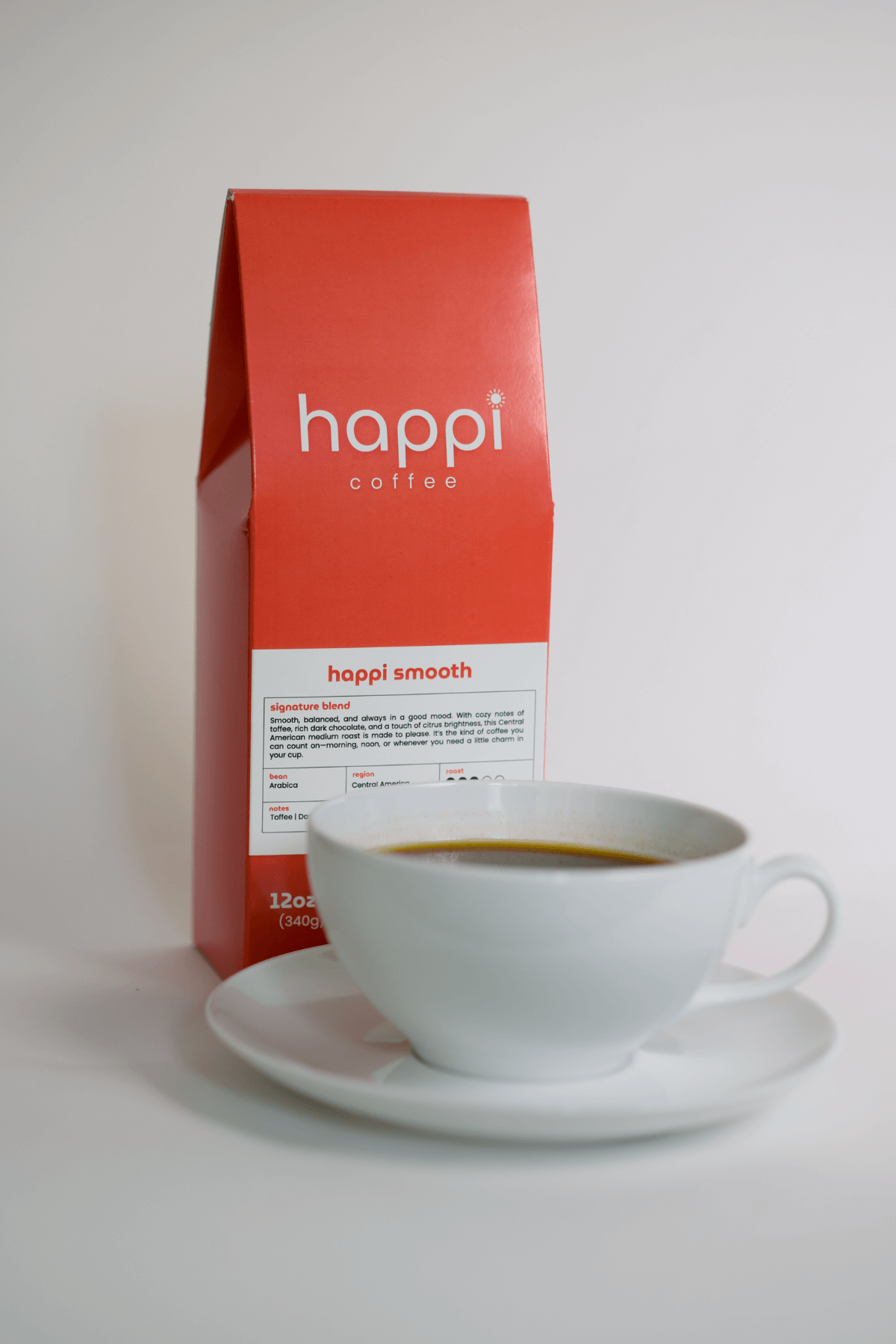 12 oz bag of Happi Smooth medium roast specialty coffee with brewed coffee in a white cup and saucer